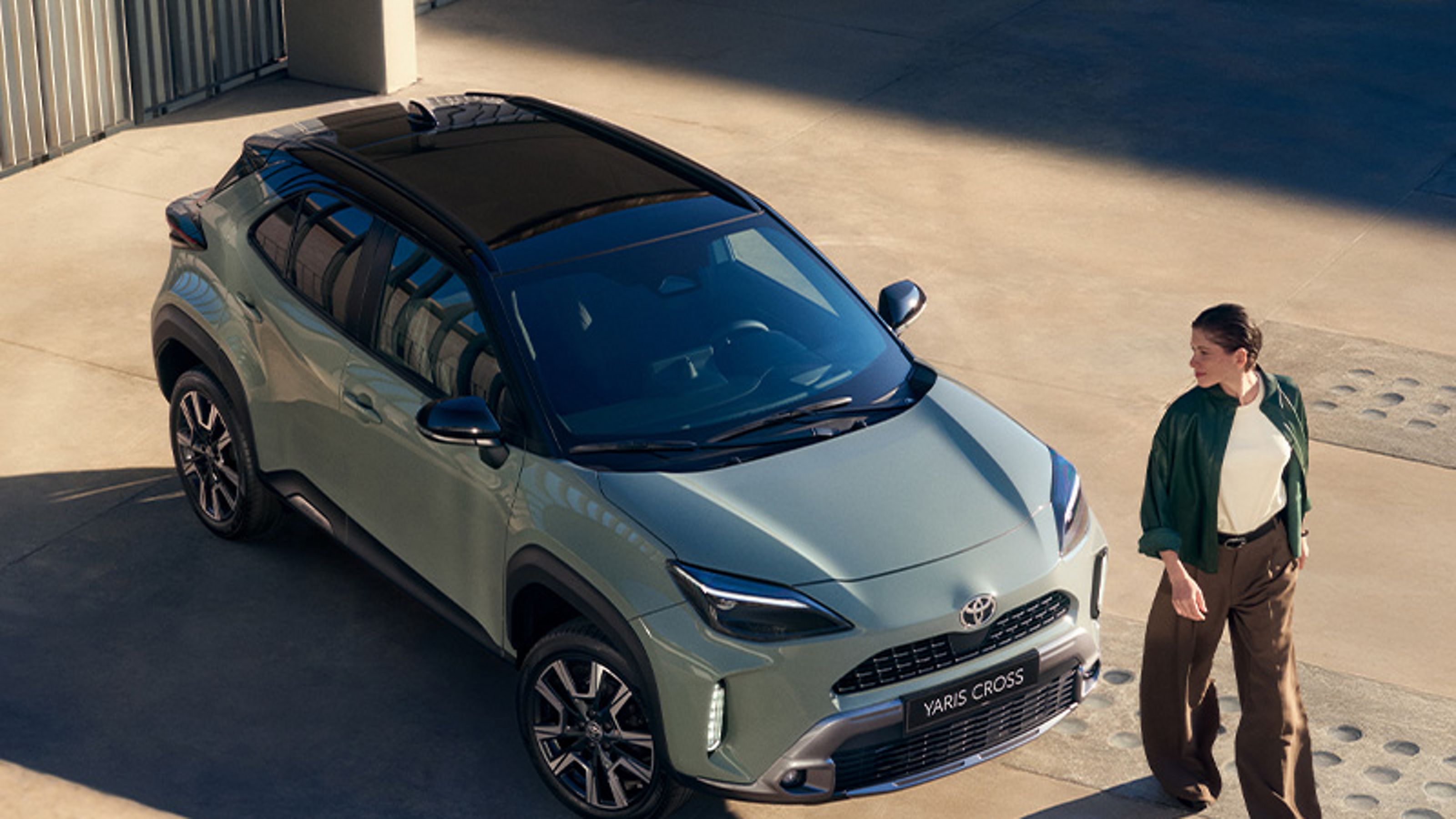 Eine Frau steht vor einem schwarz-gelben Toyota C-HR, im Hintergrund eine Wallbox.