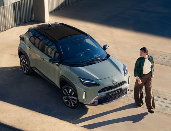 Eine Frau steht vor einem schwarz-gelben Toyota C-HR, im Hintergrund eine Wallbox.
