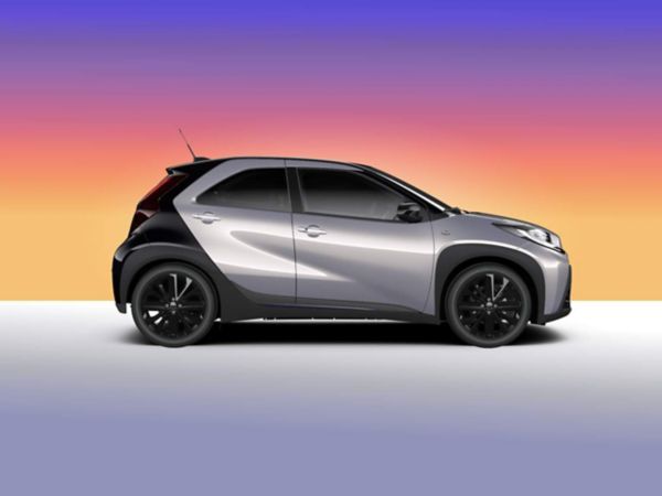 Silberner Aygo X in Seitenansicht vor Verlauf in Orange-Lila.