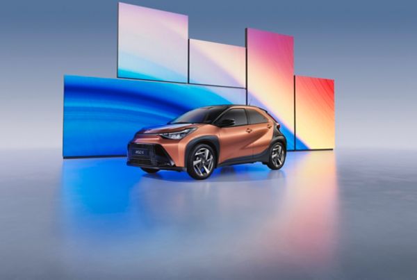 Toyota Aygo X w kolorze Cinnamon zaparkowana przed kolorowymi ekranami LED