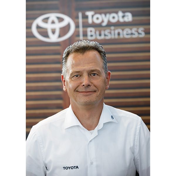 Alexander Worzfeld trägt ein Hemd mit dem Toyota-Logo und steht vor einem Hintergrund mit dem Markenzeichen: Toyota Business