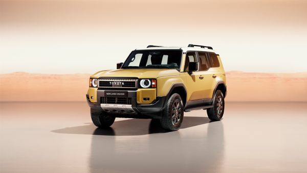 A front view of the all-new Toyota Land Cruiser parked at an angle. Its bright metallic gold paint contrasts with the orange studio setting.