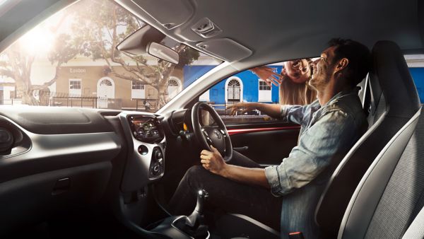 Man in Toyota Aygo X laughing while girl on the roof waves through the window