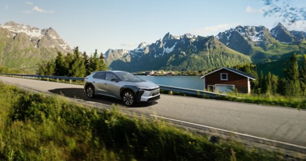 Ein silberner Toyota bZ4X fährt durch eine bergige Landschaft mit Seen und Wäldern.