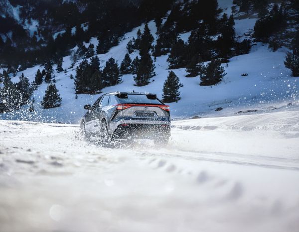 Ein Toyota bZ4X fährt durch eine Schneelandschaft in den Bergen, während er hinter sich eine Wolke aus Schnee aufwühlt.