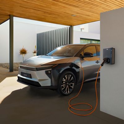 Toyota bZ4X wird an einer Wallbox vor einem modernen Wohnhaus geladen.