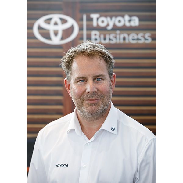 Björn Dettmann trägt ein Hemd mit dem Toyota-Logo und steht vor einem Hintergrund mit dem Markenzeichen: Toyota Business
