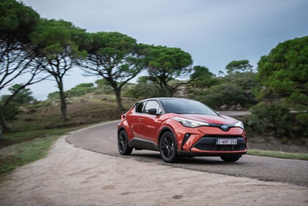 Ağaçlık bir yolda kırmızı renkli Toyota hibrit otomobil