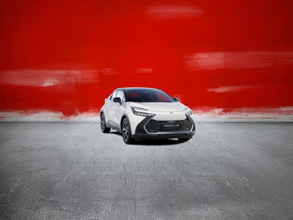 Frontansicht von einem weißen Toyota C-HR vor einer roten Wand und auf einem grauen Boden