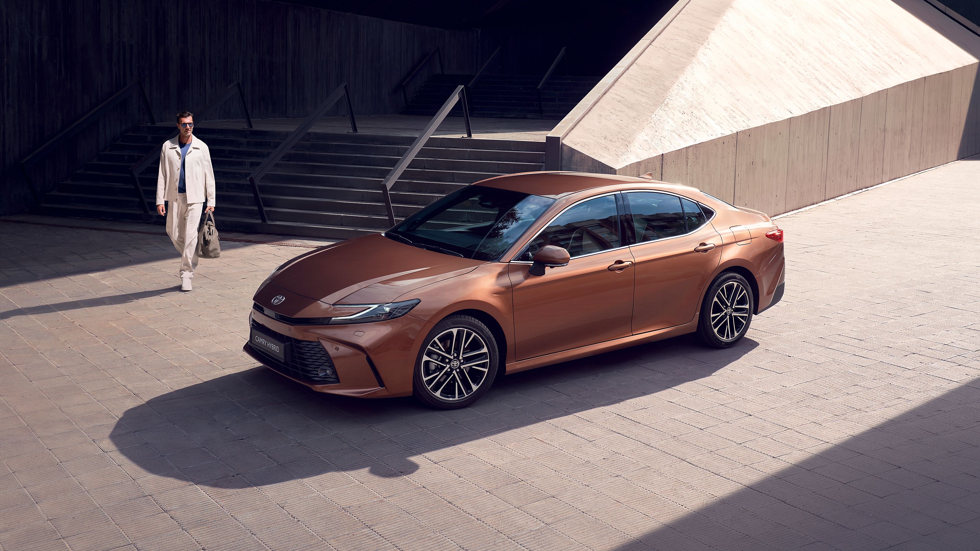 Гибридная Toyota Camry у нижней части лестницы и идущий к ней человек.