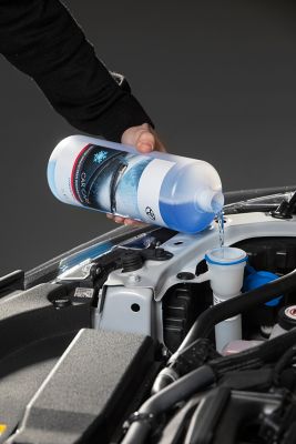 Nahaufnahme einer Flasche mit blauer Flüssigkeit, die in einen Trichter in einer offenen Motorhaube gegossen wird