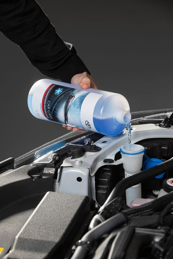 Nahaufnahme einer Flasche mit blauer Flüssigkeit, die in einen Trichter in einer offenen Motorhaube gegossen wird