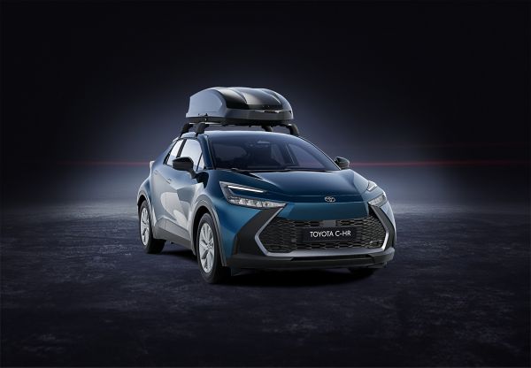 Rückansicht eines dunkelgrauen Toyota C-HR mit montiertem Fahrradträger auf der Anhängerkupplung in einer leeren Halle mit dunklem Boden und Wänden