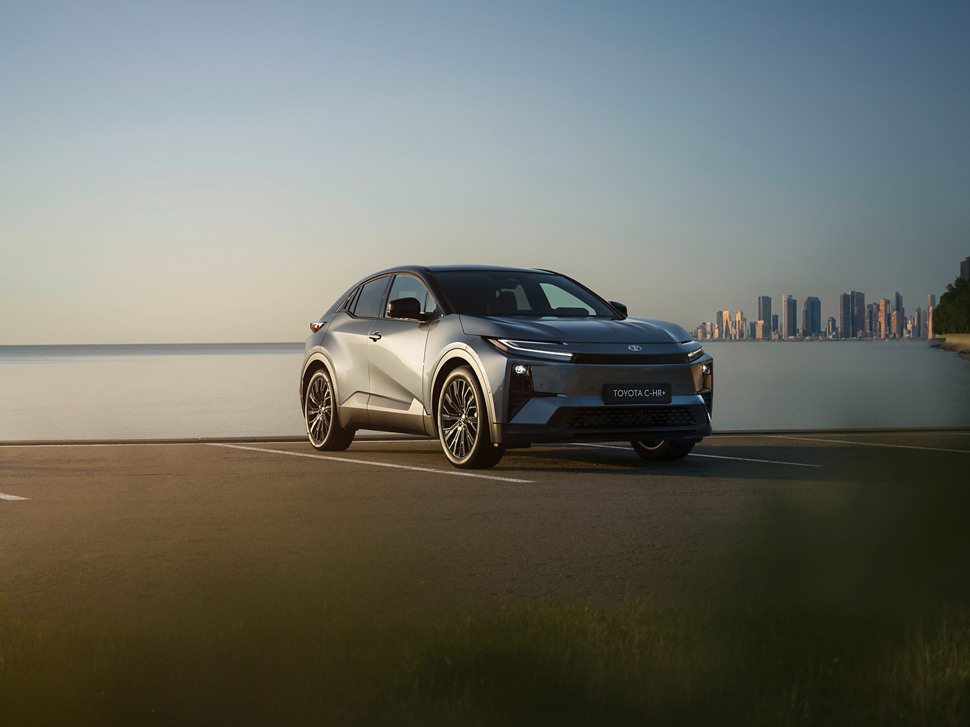 Toyota C-HR+ set against a scenic viewpoint with a city skyline in the background.