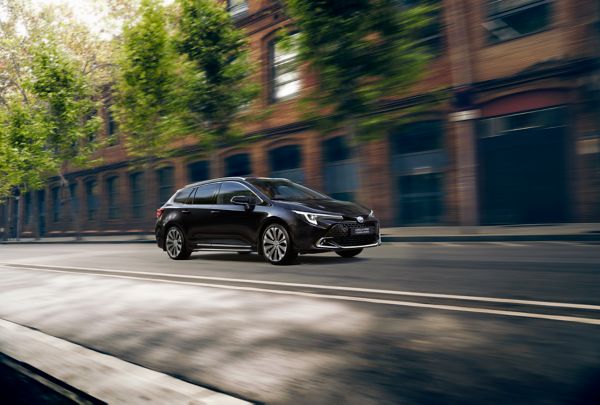 Ein schwarzer Corolla Touring Sports fährt durch eine von Bäumen gesäumten Straßen einer Altstadt.