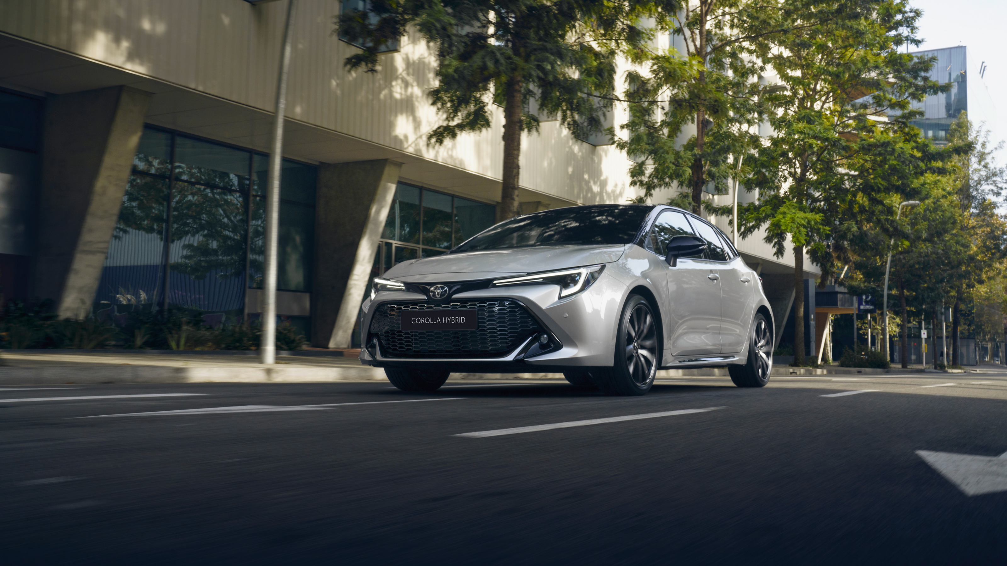 Toyota Corolla Hatchback drives along a leafy urban street