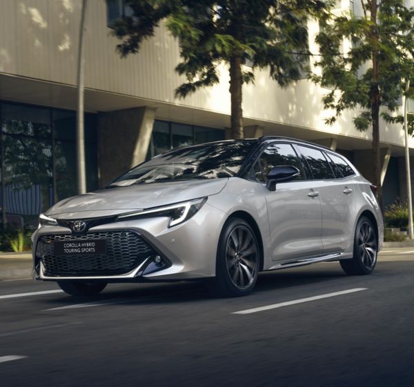 A Toyota Corolla Touring Sports drives past a modern city building