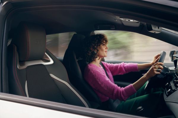 Person in violettem Oberteil fährt lächelnd im Auto