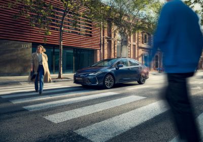 Yaya geçidinden geçen iki insan ve bekleyen Toyota Corolla Hybrid araç