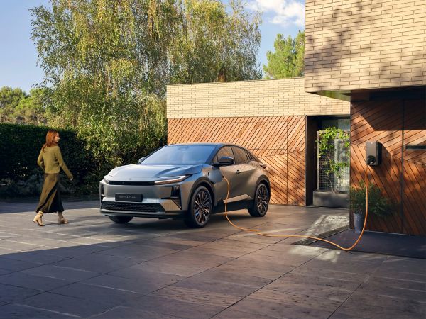 A Toyota C-HR+ charges outside a modern and striking-looking home