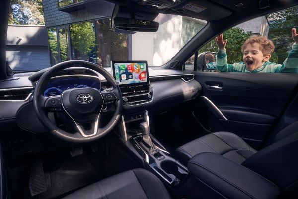 Camına ellerini ve yüzünü yapıştırmış küçük bir çocuk bulunan Toyota Corolla Cross Hybrid iç görünümünde direksiyon, multimedya ekran ve vites