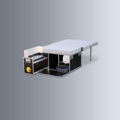 Campingbox mit ausziehbarer Kochstelle und ausgeklappter Liegefläche.