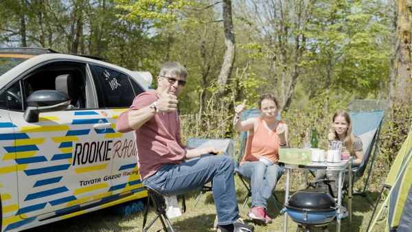 Zwei Camper sitzen auf Klappstühlen und strecken ihren Daumen in die Kamera