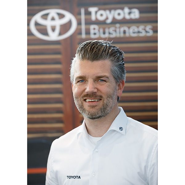 Christian Selbach trägt ein Hemd mit dem Toyota-Logo und steht vor einem Hintergrund mit dem Markenzeichen: Toyota Business