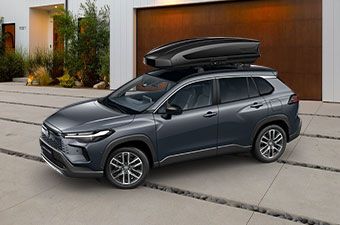 Toyota Corolla Cross z boksem dachowym stoi przed zamkniętym garażem domu.