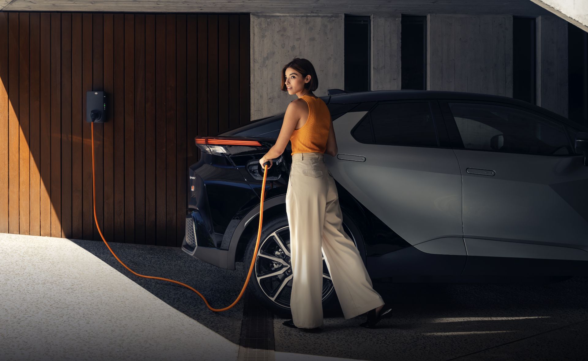 Kobieta ładuje Toyotę za pomocą kabla ze stacji domowej w garażu.