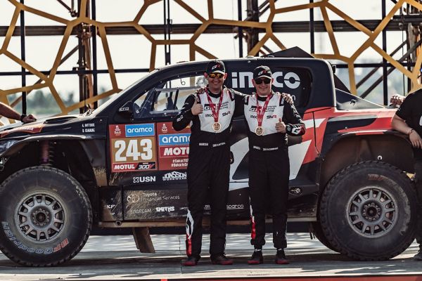 Toyota dakar ralli aracı yanında poz veren iki sporcu