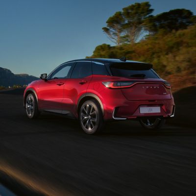 Ein eleganter roter Lexus LBX, der auf einer kurvenreichen Straße fährt, umgeben von Grünflächen und Bergen im Hintergrund
