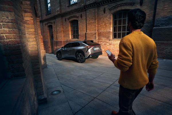 A man sits in the driver's seat of a Toyota car holding his smartphone. The phone displays the TOYOTA MyToyota app logo.