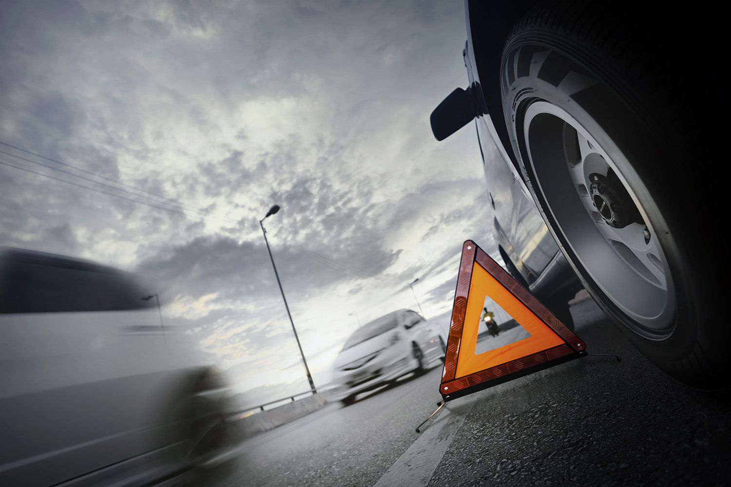 Zbliżenie na trójkąt ostrzegawczy obok koła pojazdu na drodze.