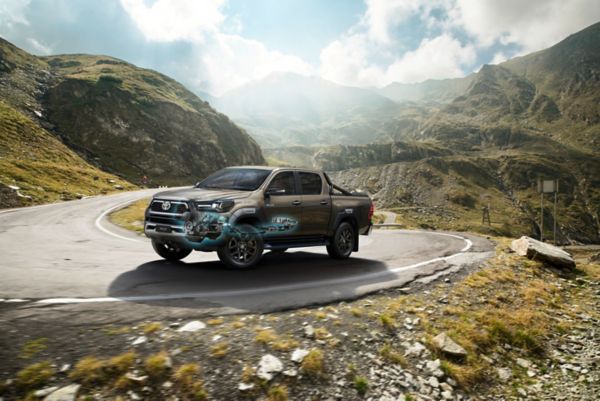 Ein robuster Pickup-Truck fährt eine kurvenreiche Bergstraße entlang, umgeben von üppigen Hügeln und einem bewölkten Himmel. Das Fahrzeug steht für Abenteuergeist und Geländetauglichkeit.