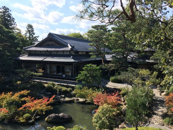 Ein ruhiger japanischer Garten mit einem Haus im traditionellen Stil, umgeben von üppigem Grün und buntem Herbstlaub