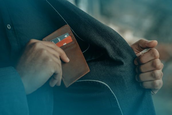 Eine Person, die diskret eine braune Brieftasche mit sichtbaren Kreditkarten in ihre Jackentasche steckt, was auf einen Fokus auf persönliche Sicherheit hindeutet.