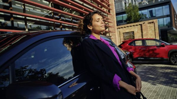 Une femme souriante adossé à une voiture