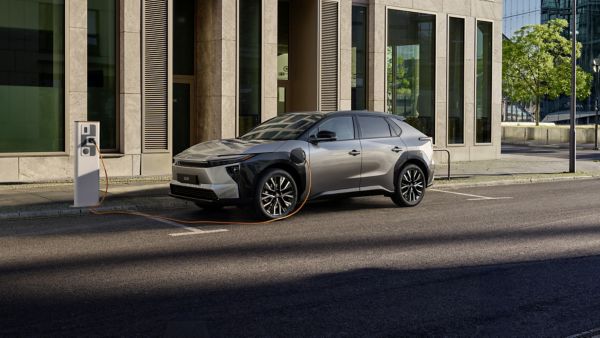 Toyota bZ4X electric SUV parked on an urban street beside an EV chargepoint. Man holds an EV cable at the front of the car.