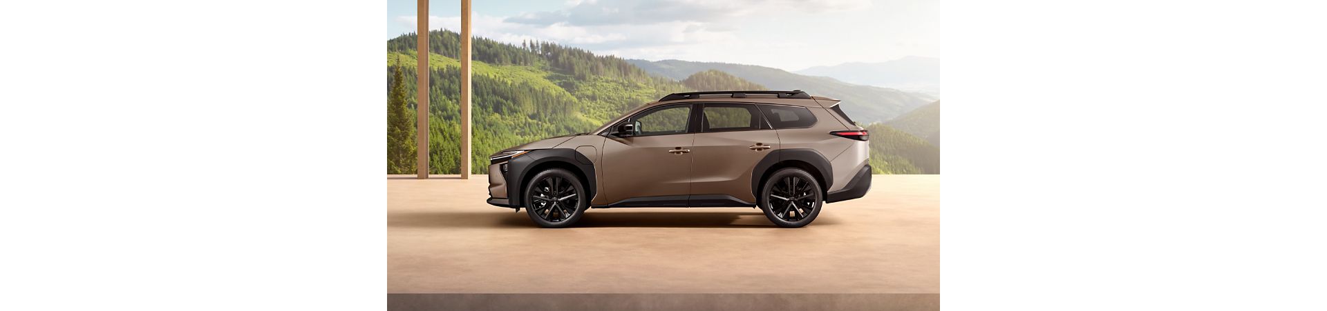 Profil bronzového SUV Toyota bZ4X Touring zaparkovaného na dřevěné podlaze. V pozadí je vidět horská a lesní krajina. 