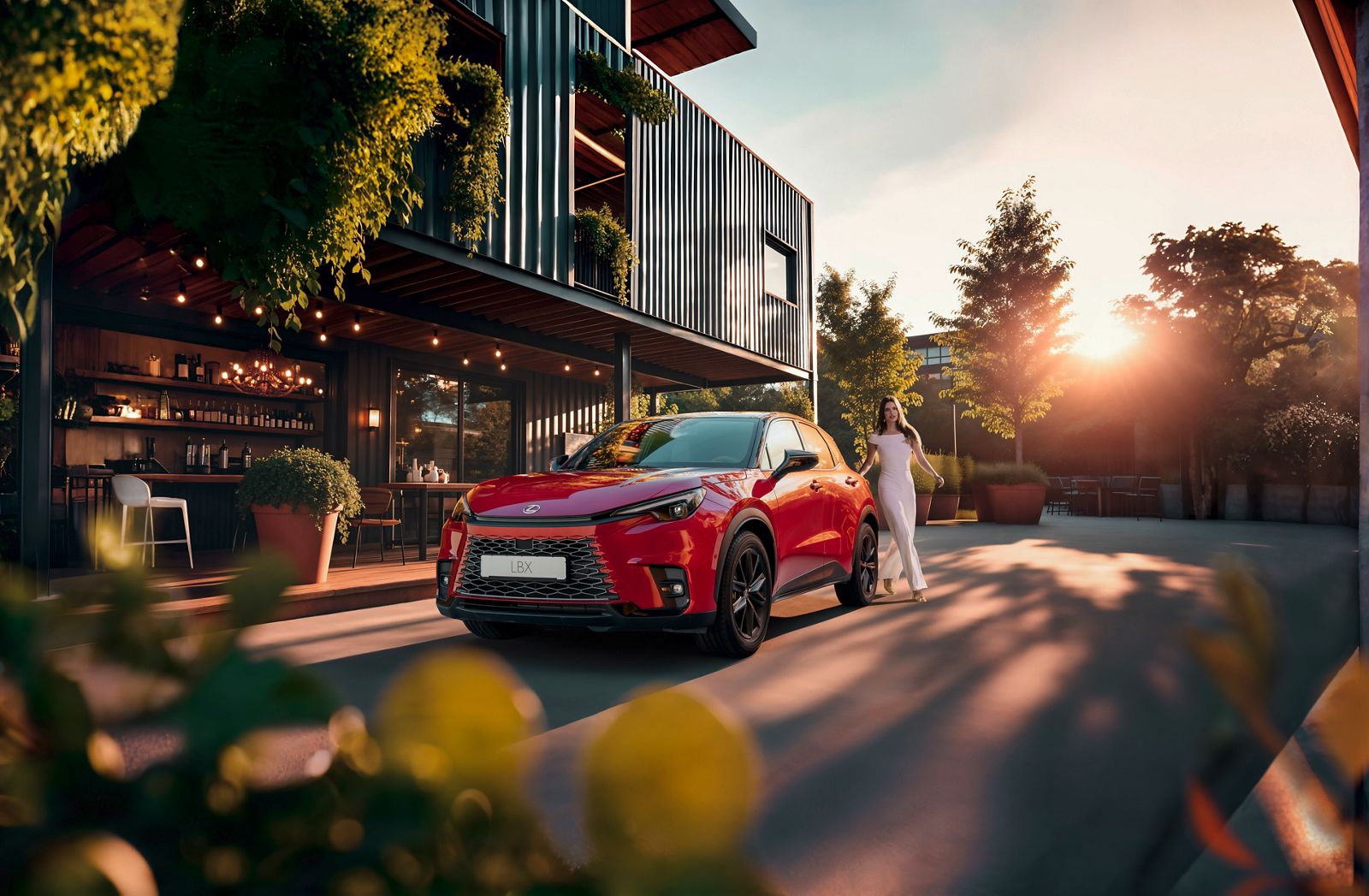 Roter Lexus SUV steht vor einem modernen Gebäude mit großen Glasfronten und grünen Pflanzen, während eine Person daneben steht; die Szene ist in warmes Sonnenlicht getaucht.