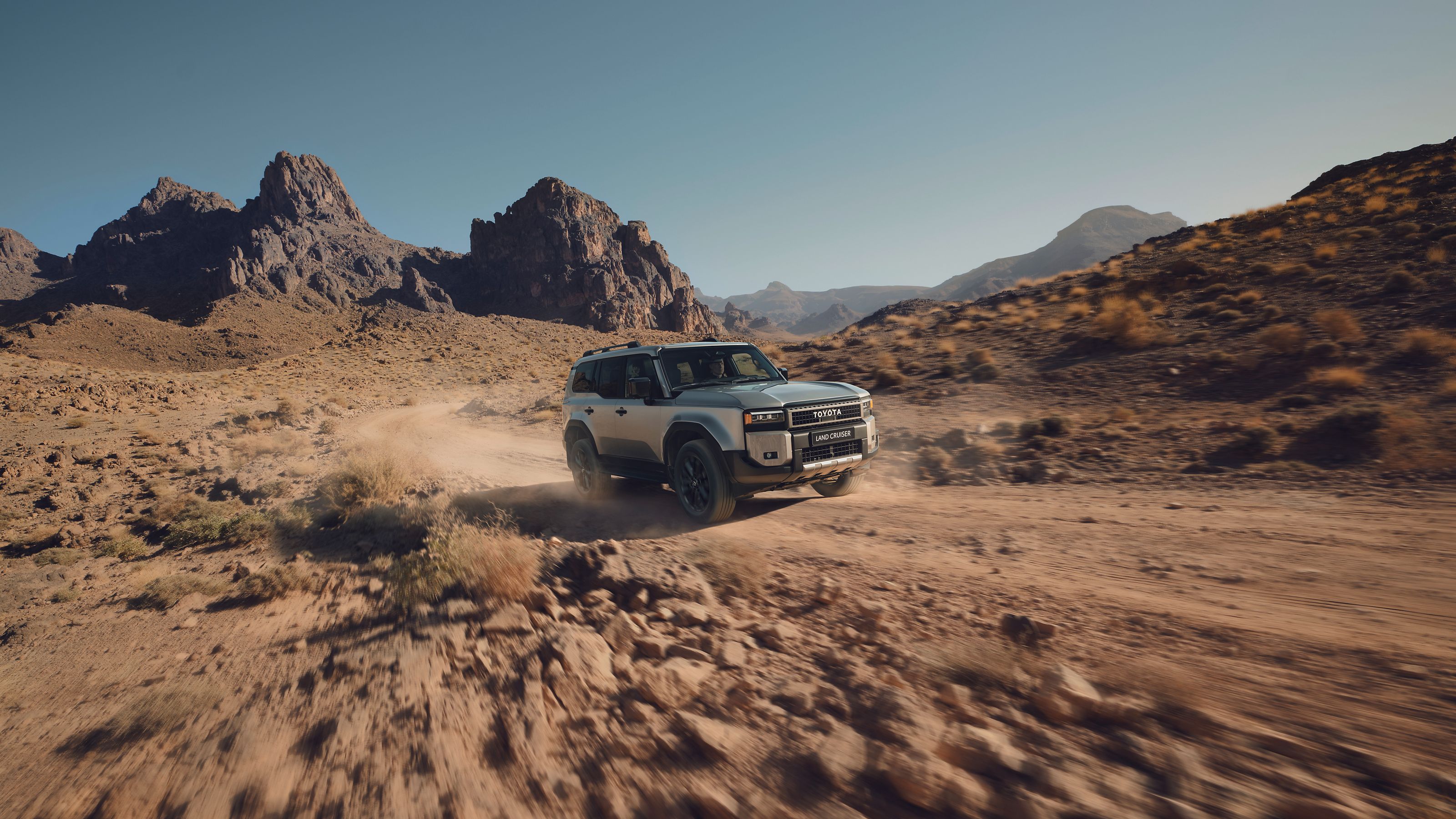 A Toyota Land Cruiser drives through a desert landscape