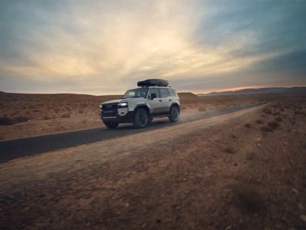 Land Cruiser mit installiertem Gepäckträger fährt auf einer unbefestigten Straße in einer Wüste entlang.