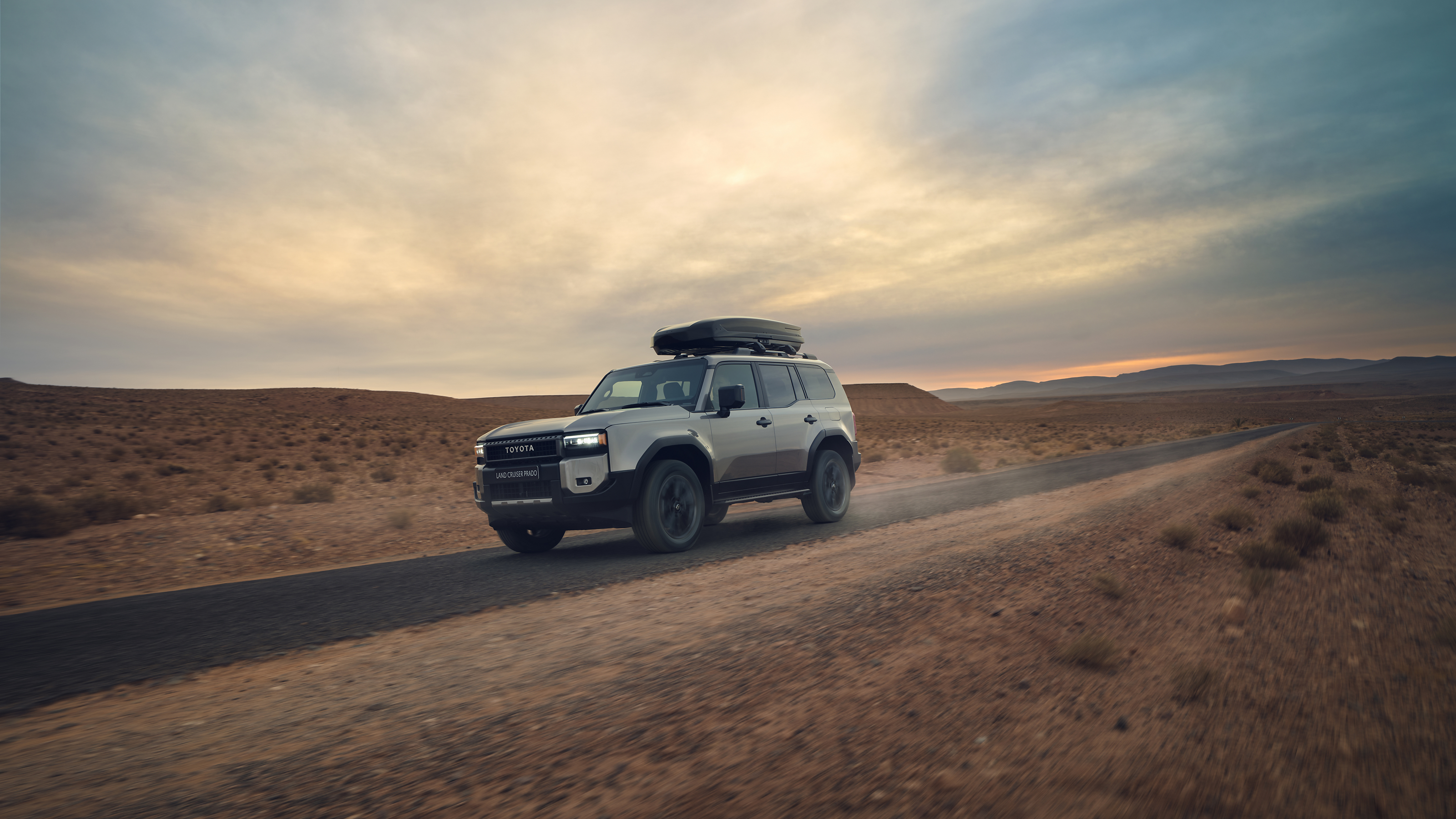 A Land Cruiser equipped with a Toyota roofbox drives through the desert