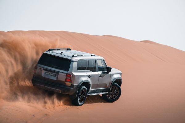 Silberner Land Cruiser fährt über eine Düne und wirbelt hinter sich eine Wolke von Sand auf.