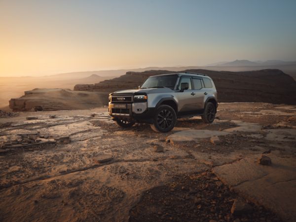 A front view of the all-new Toyota Land Cruiser parked at an angle. Its bright metallic gold paint contrasts with the orange studio setting.