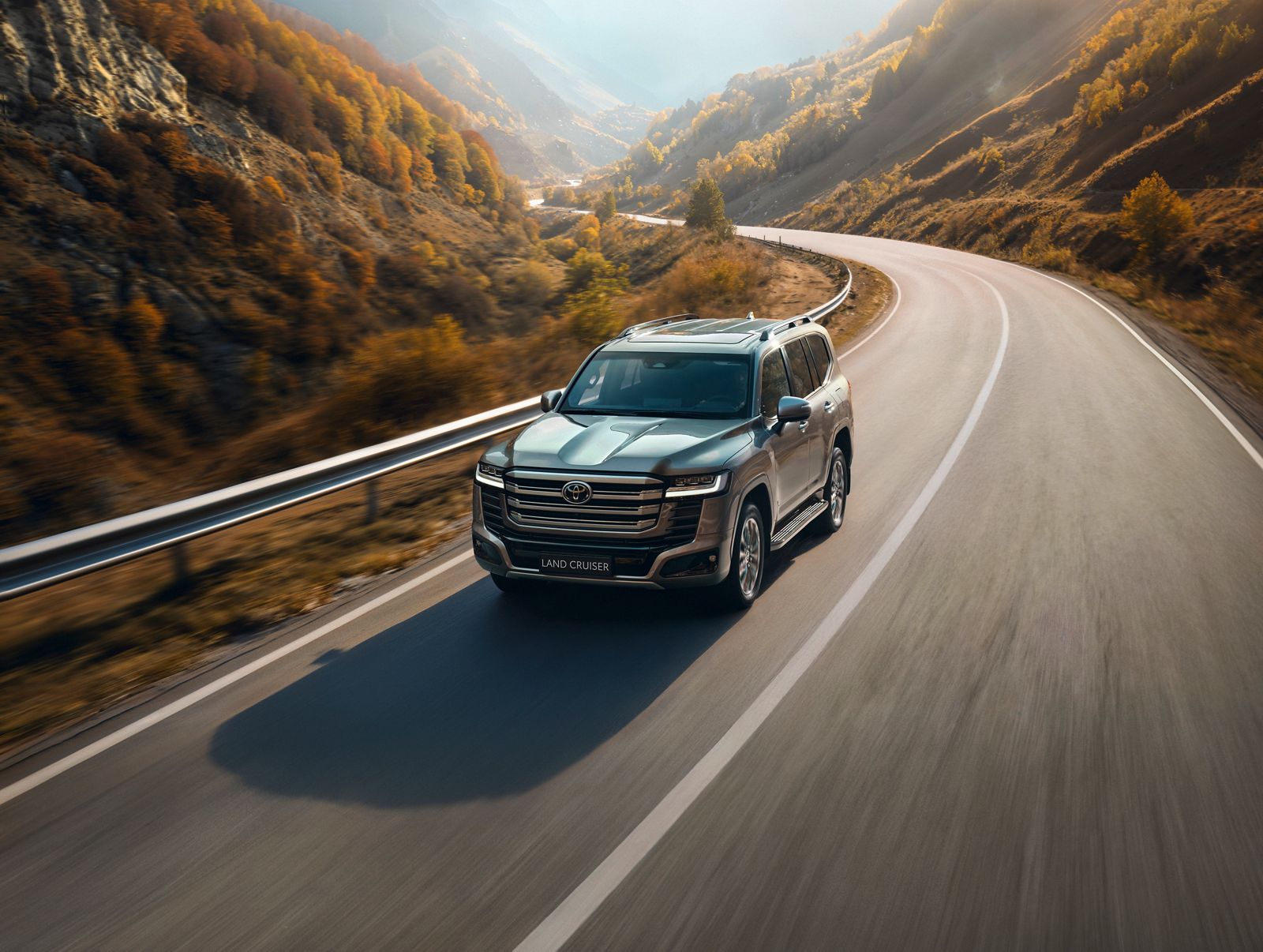 Land Cruiser 300 driving on a sunlit mountain road.
