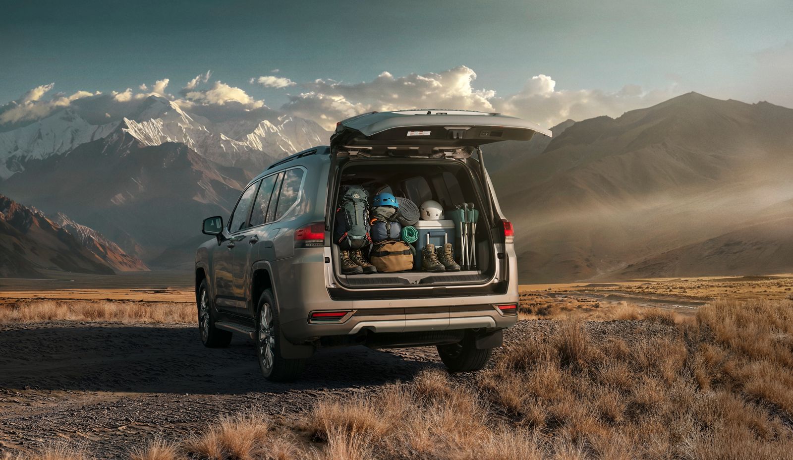 Land Cruiser 300 parked with open tailgate, gear loaded, ready for adventure beneath rugged mountains.