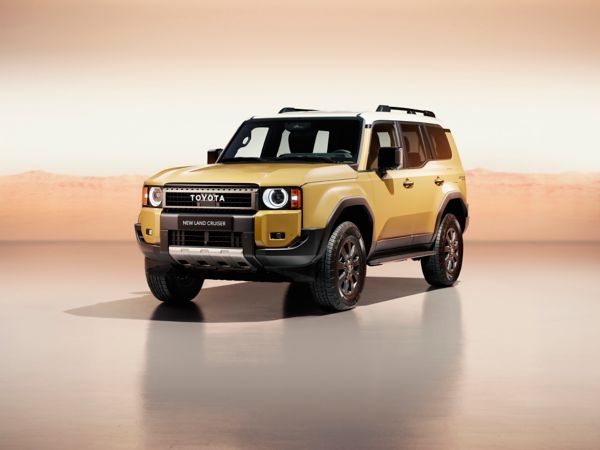 A front view of the all-new Toyota Land Cruiser parked at an angle. Its bright metallic gold paint contrasts with the orange studio setting.