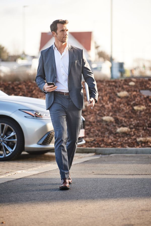 A person in a suit and tie walks with a cell phone, representing Lexus Business Leasing.